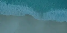 Aerial view of a gentle wave washing onto a sandy shore.